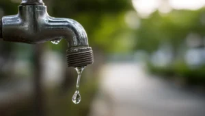 Water dripping from an old metal faucet in the backyard with a blurred green background, emphasizing the importance of irrigation water conservation